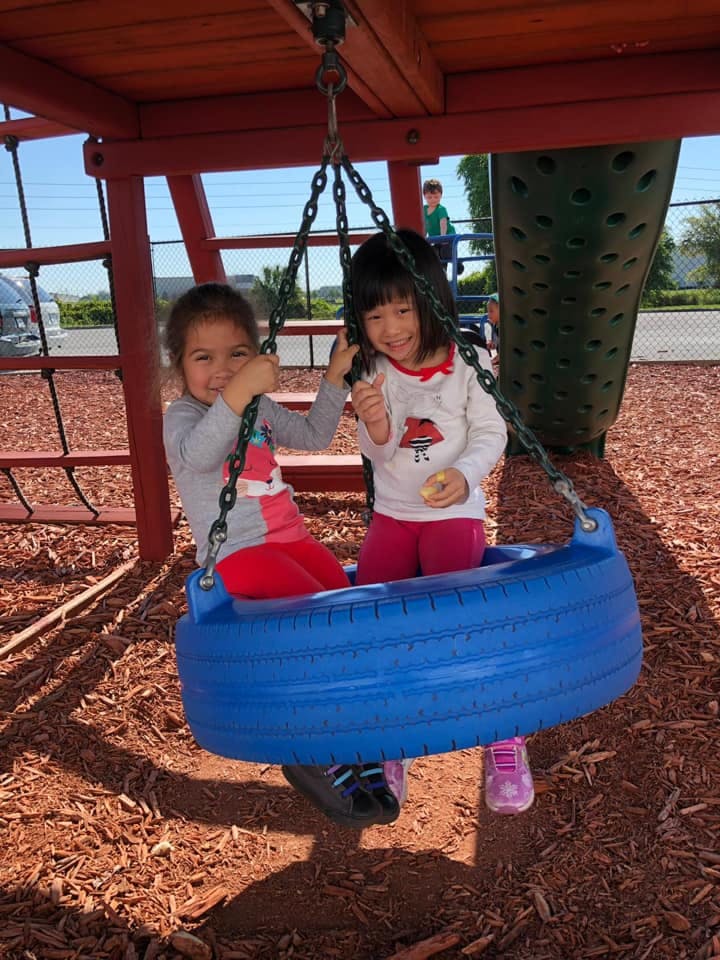 Two children on a tire swing at a playground