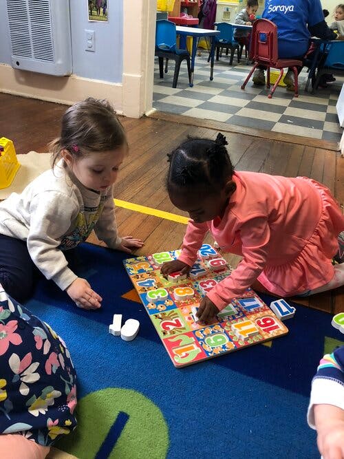 Two children playing with a number puzzle on a rug