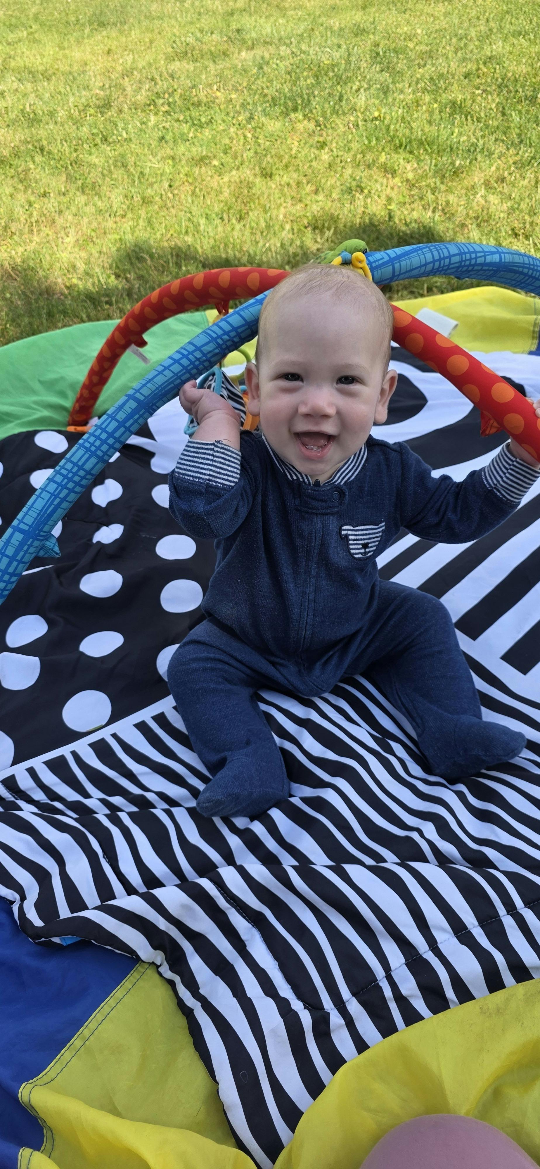 Child sitting on a playmat, holding onto toy bars and smiling