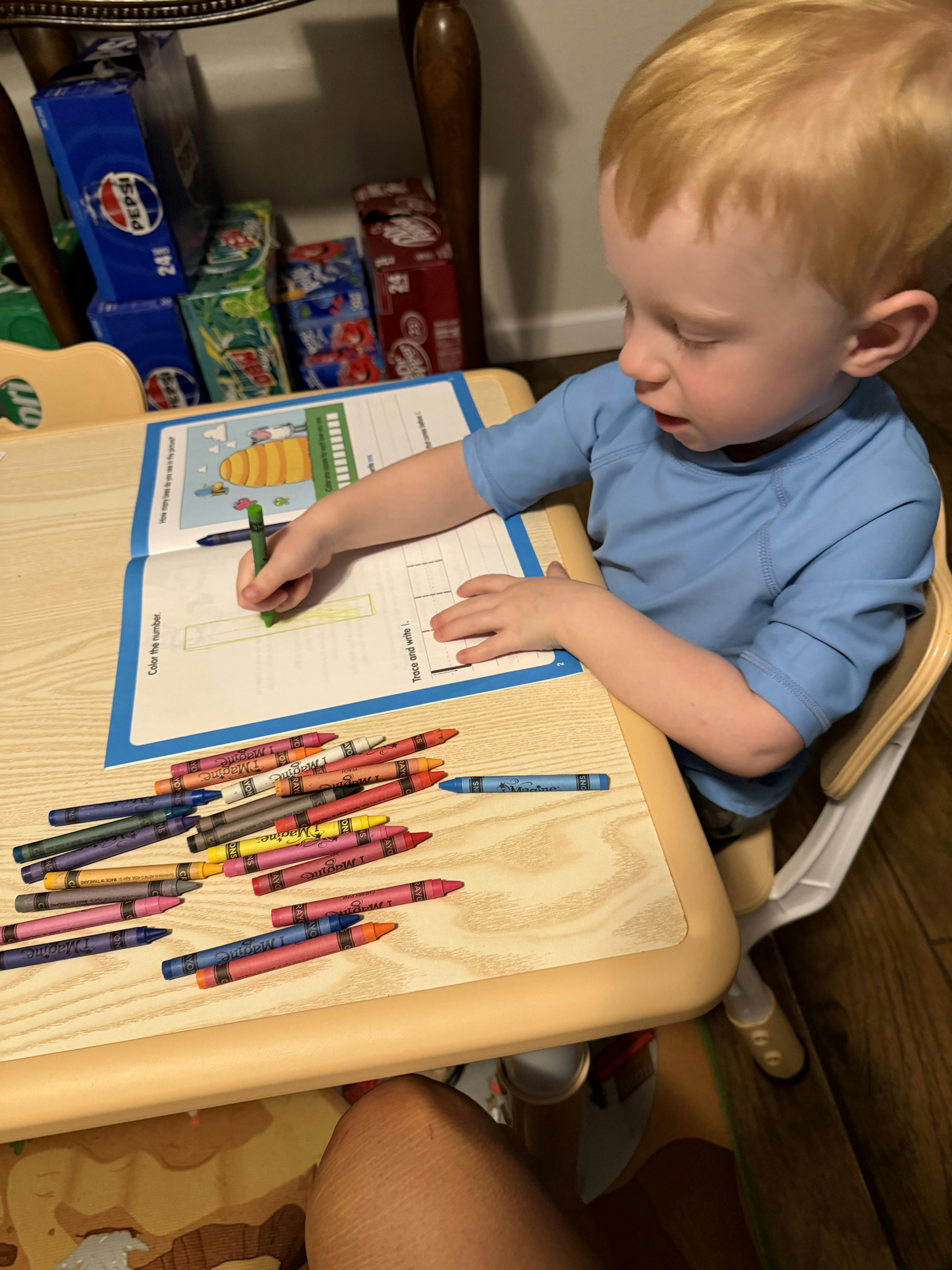 Child sitting at a table coloring in a workbook with crayons