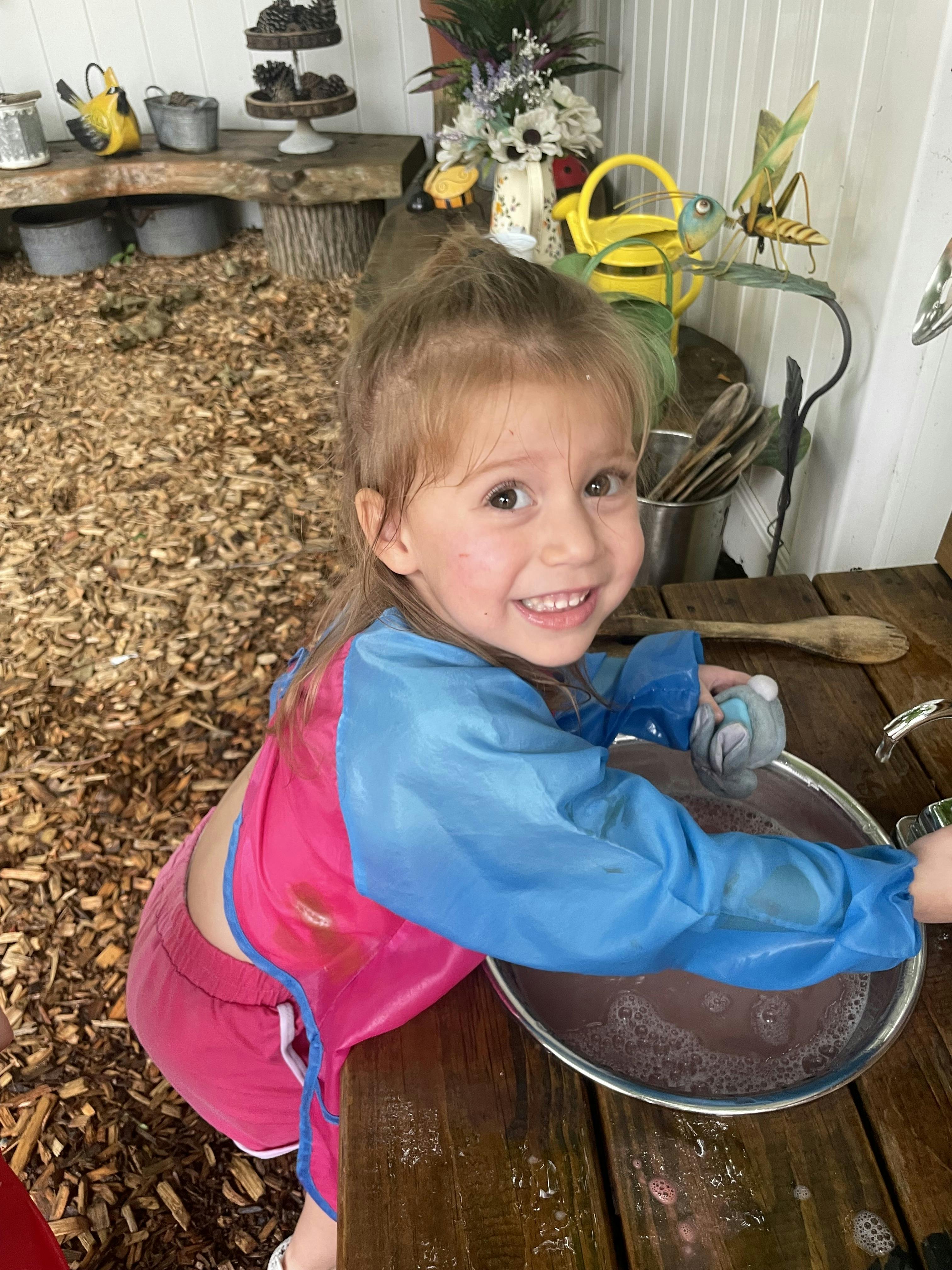 Child in an apron washing dishes in a basin
