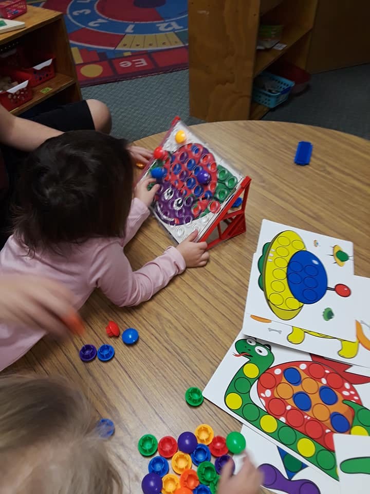 Child playing with a colorful pegboard toy on a wooden table