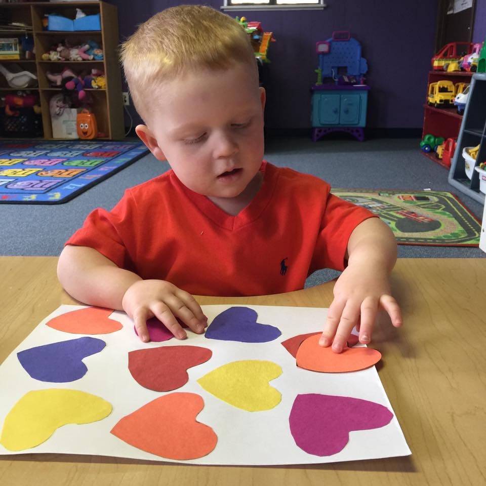 Child playing with colorful heart cutouts on a table