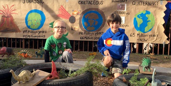 Two children kneeling in front of a banner with drawings of Earth