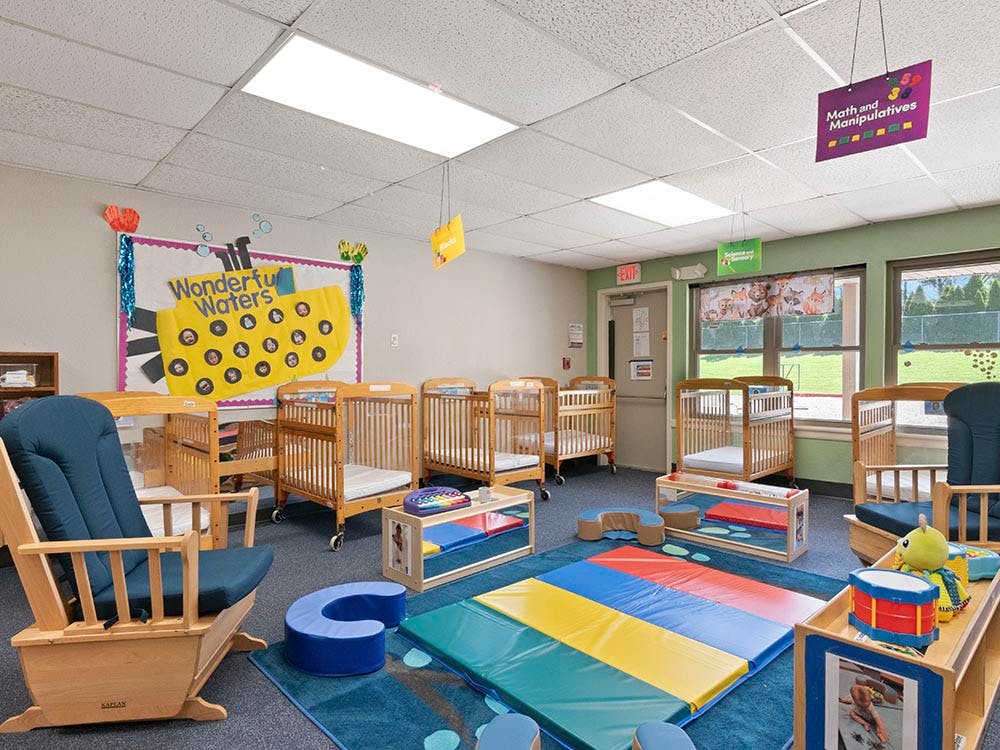 Empty nursery with several cribs, rocking chairs, and play mats