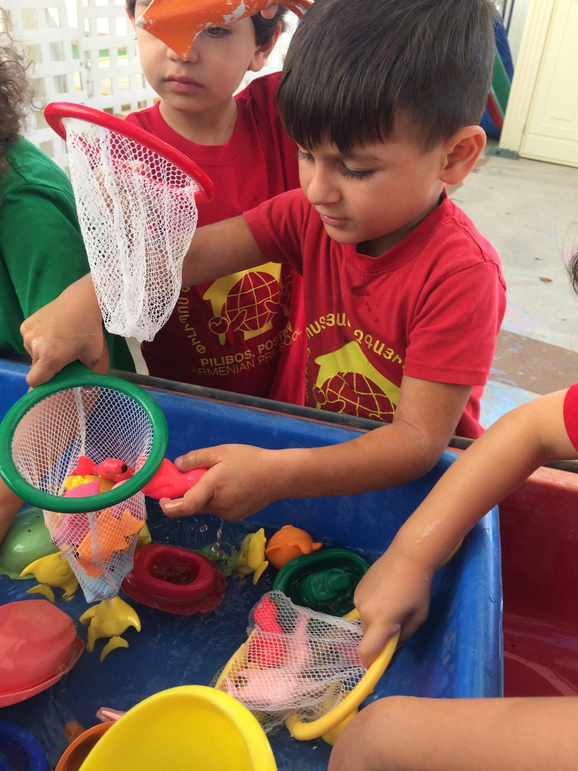 Child playing with a net and toys in a water table