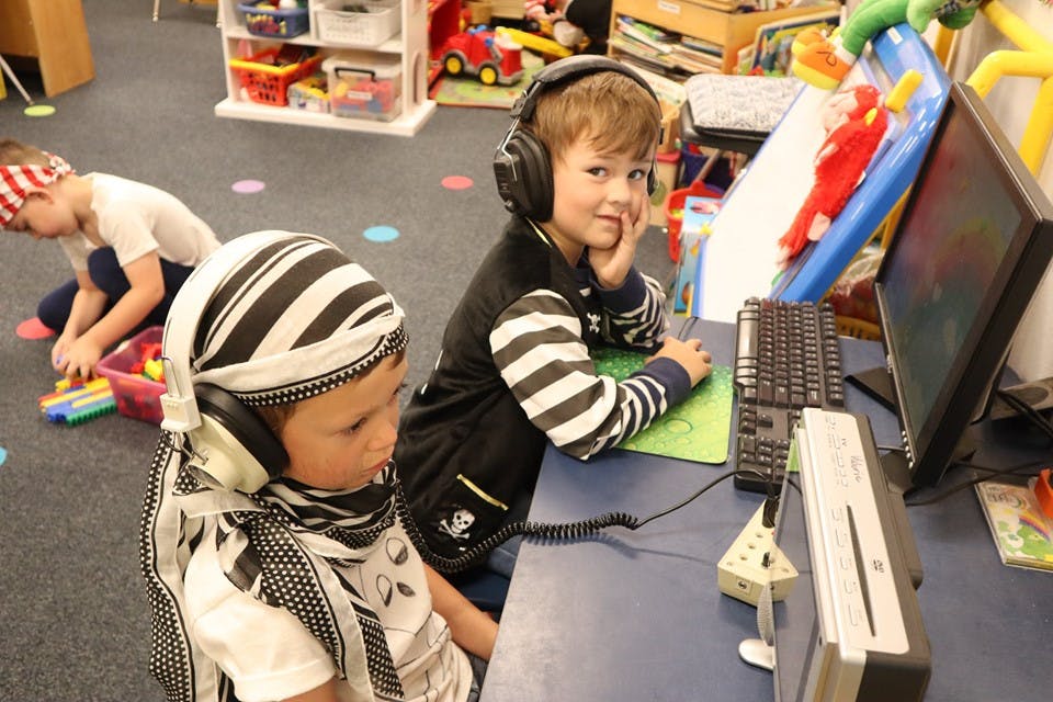 Two children wearing headphones at a desk with a computer