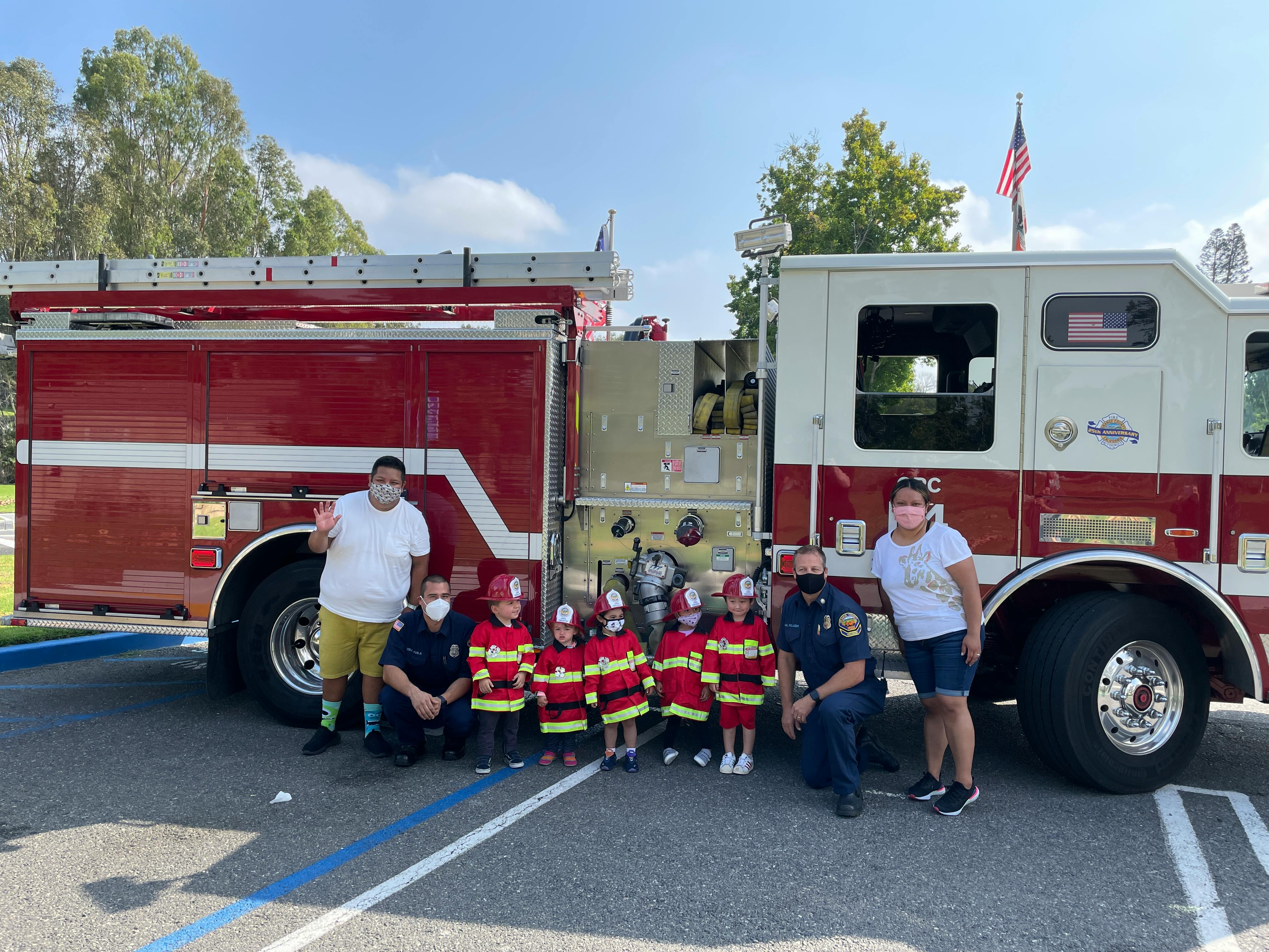 Adults and children in firefighter costumes posing in front of a fire truck