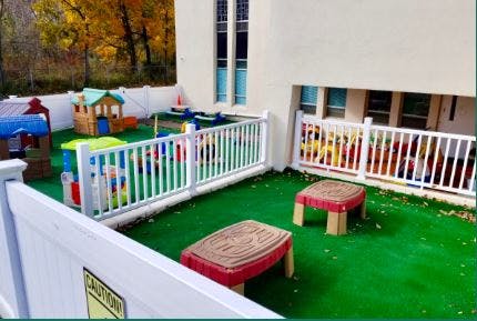 Outdoor play area with artificial turf, white fences, and colorful play structures