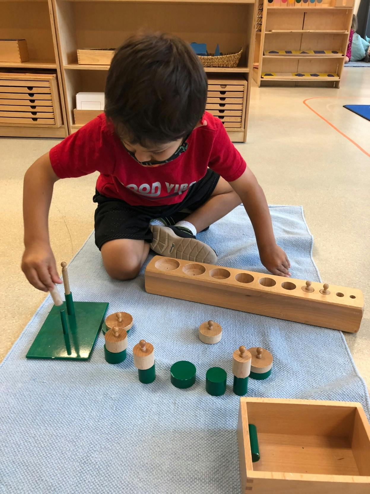 Child playing with wooden and green cylinder blocks on a mat