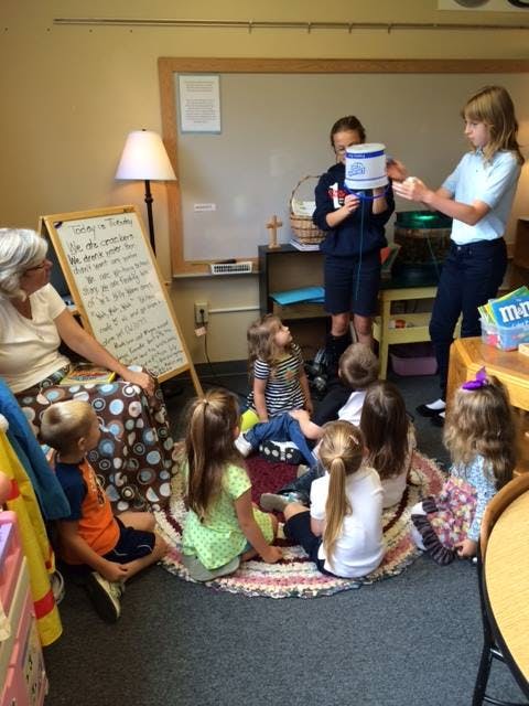 Adult and children in a classroom, two teens demonstrating to younger children