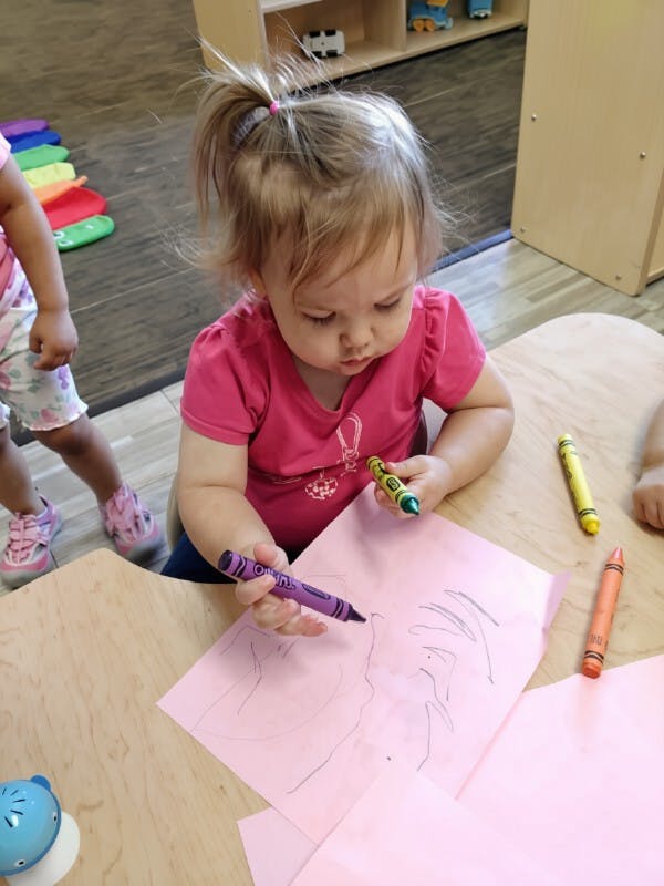 Child drawing on pink paper with a crayon at a table