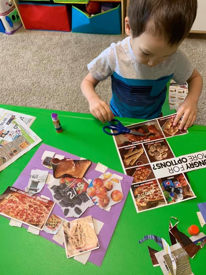 Child cutting out pictures from a magazine at a green table