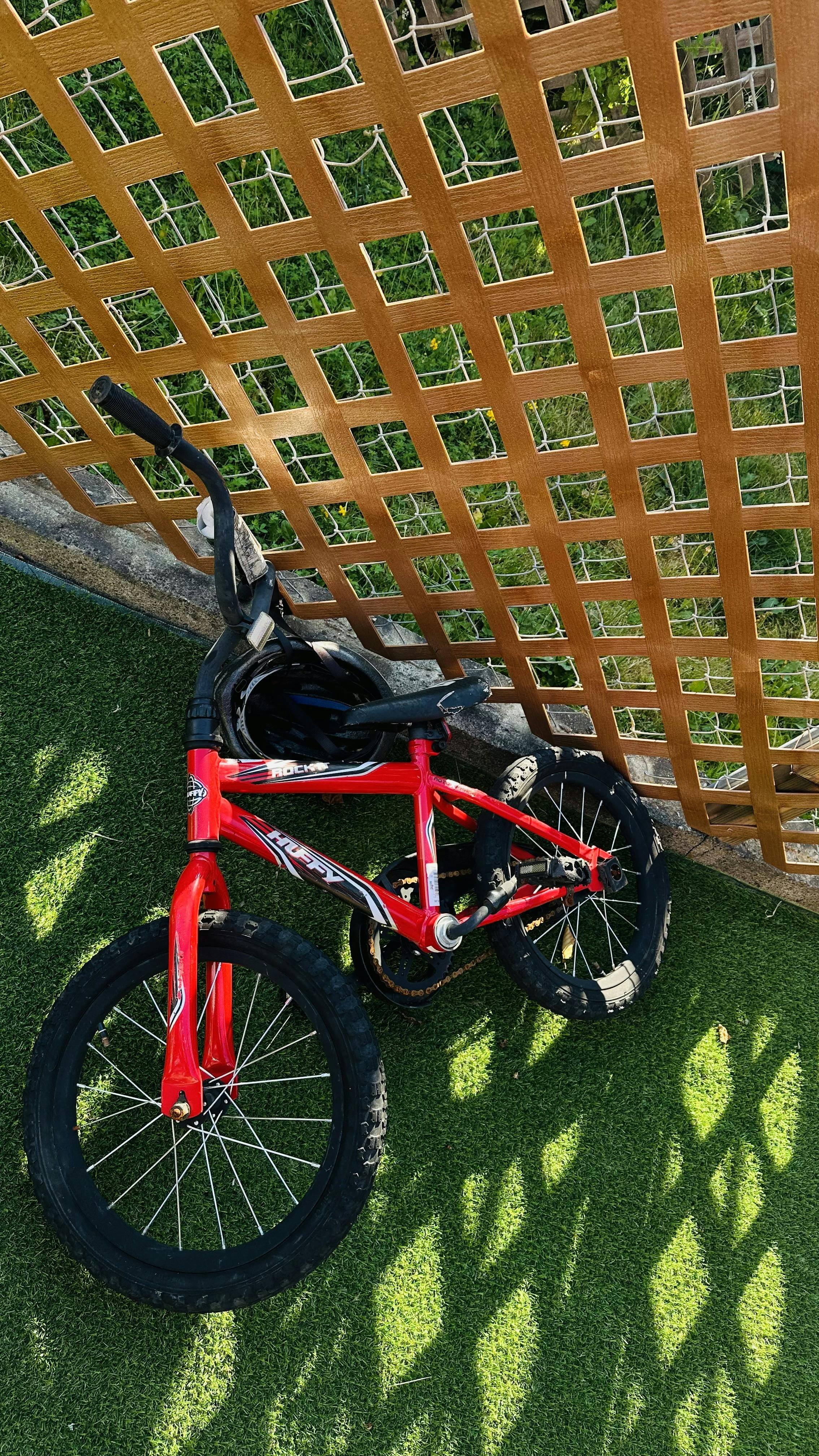 Red child bicycle leaning against a garden lattice fence