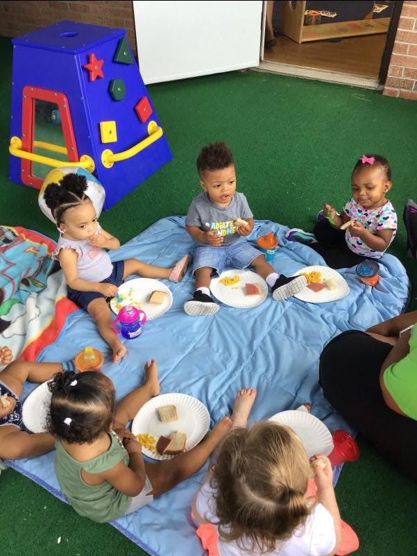 Children sitting on a blue blanket eating snacks
