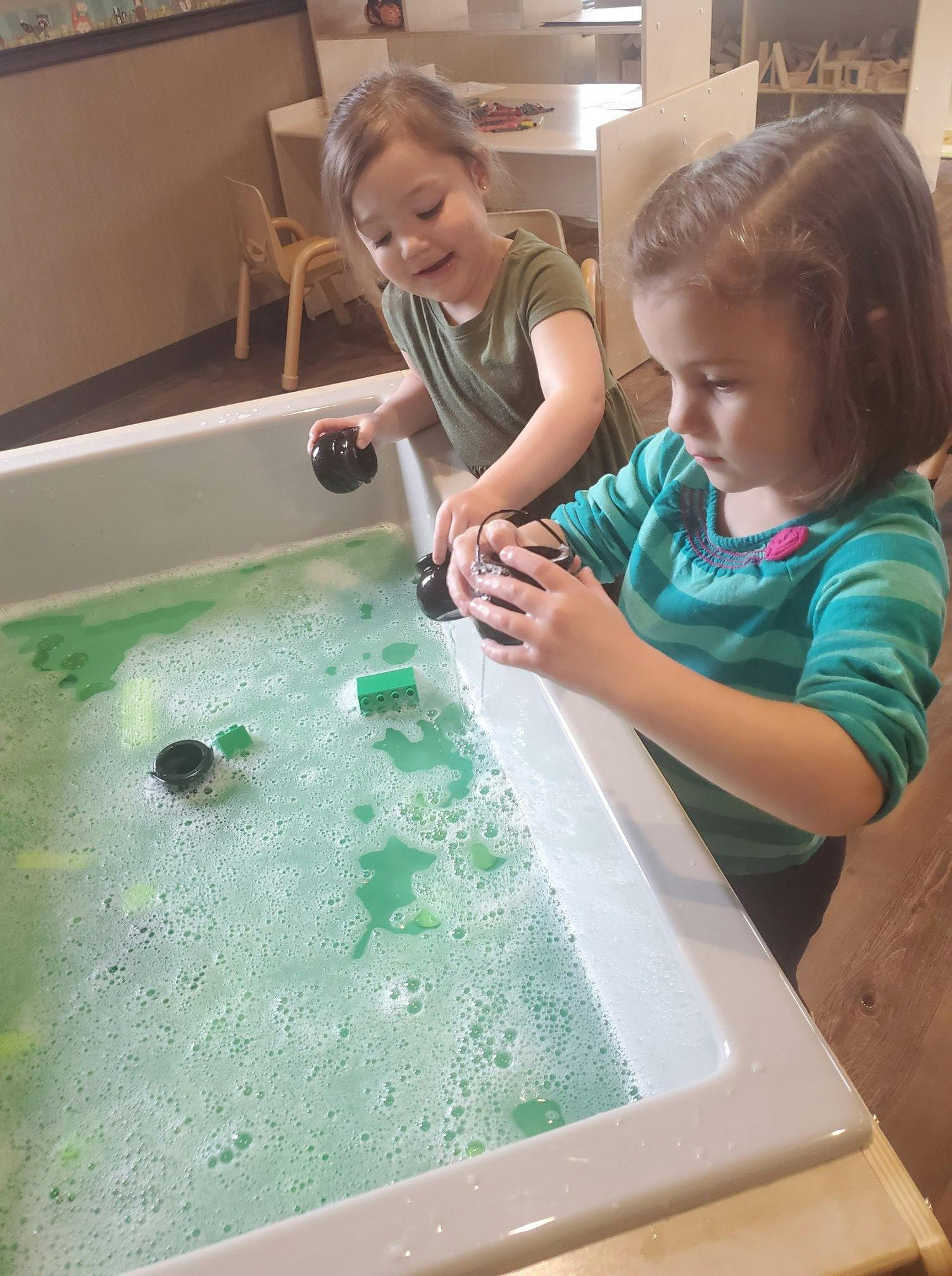 Two children playing with toys in a tub of green bubbly water