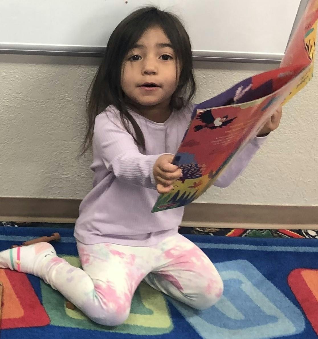 Child kneeling on a rug, holding an open book