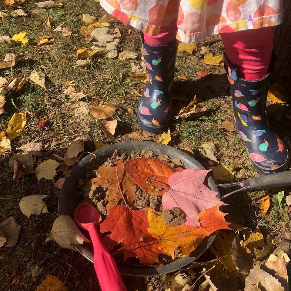 Child in rain boots standing over a pan of leaves and dirt