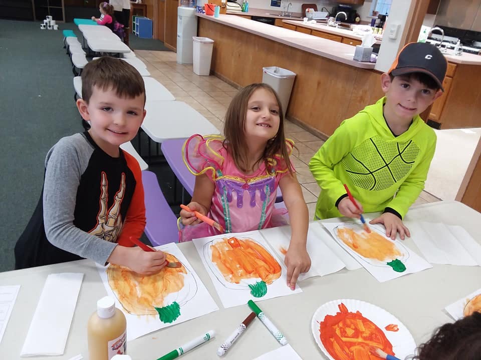 Three children painting pumpkins on paper at a table