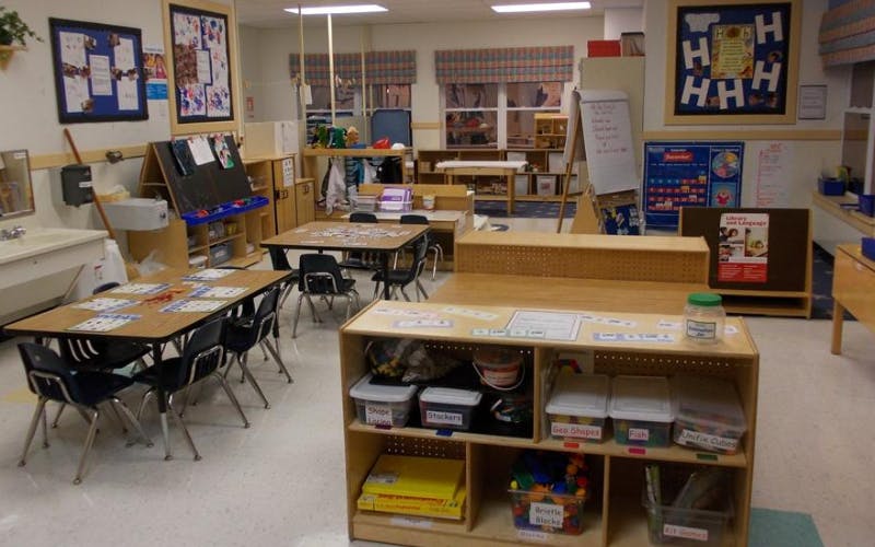 Empty classroom with small tables and chairs, shelves with toys