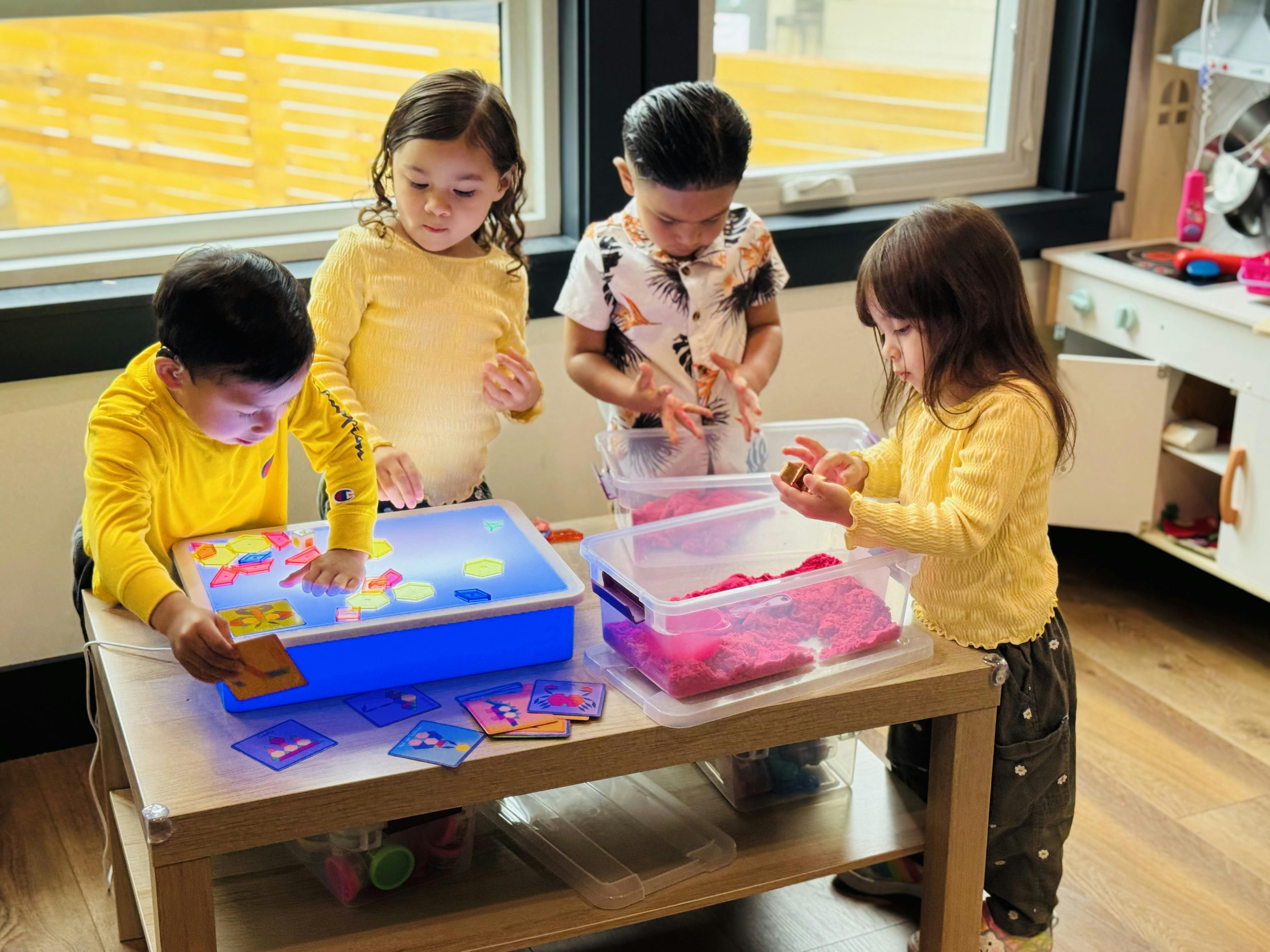 Four children playing with sensory bins and a light table
