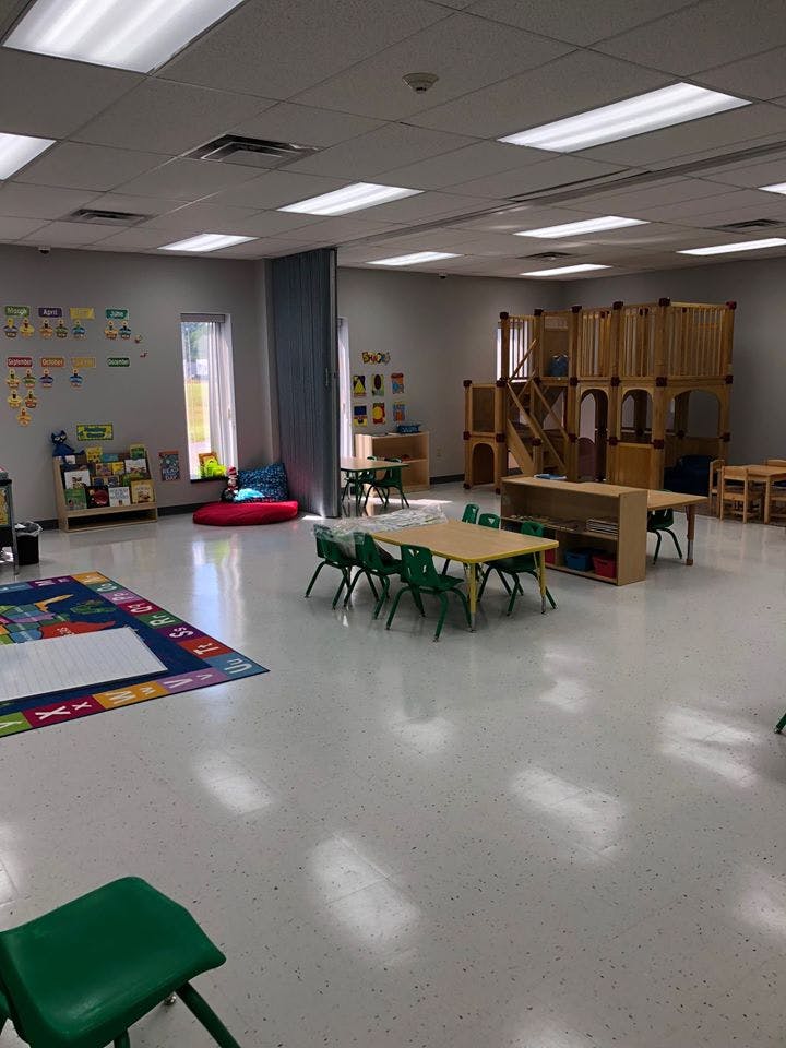 Empty classroom with small tables, chairs, and a wooden play structure
