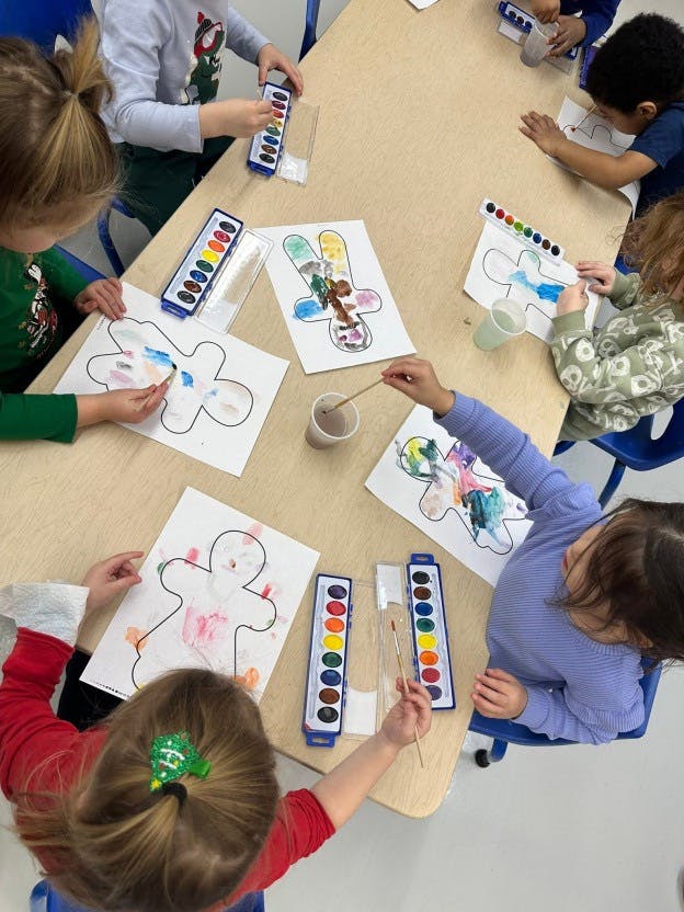 Children painting paper gingerbread shapes at a classroom table