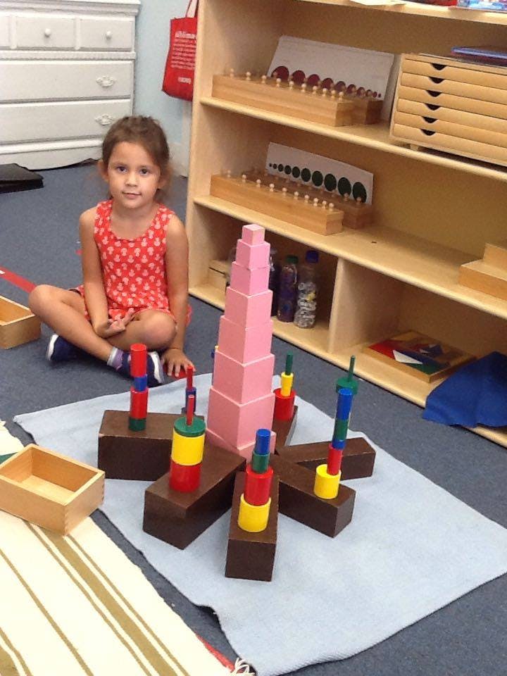 Child sitting on floor next to a tall pink block tower and other colorful blocks