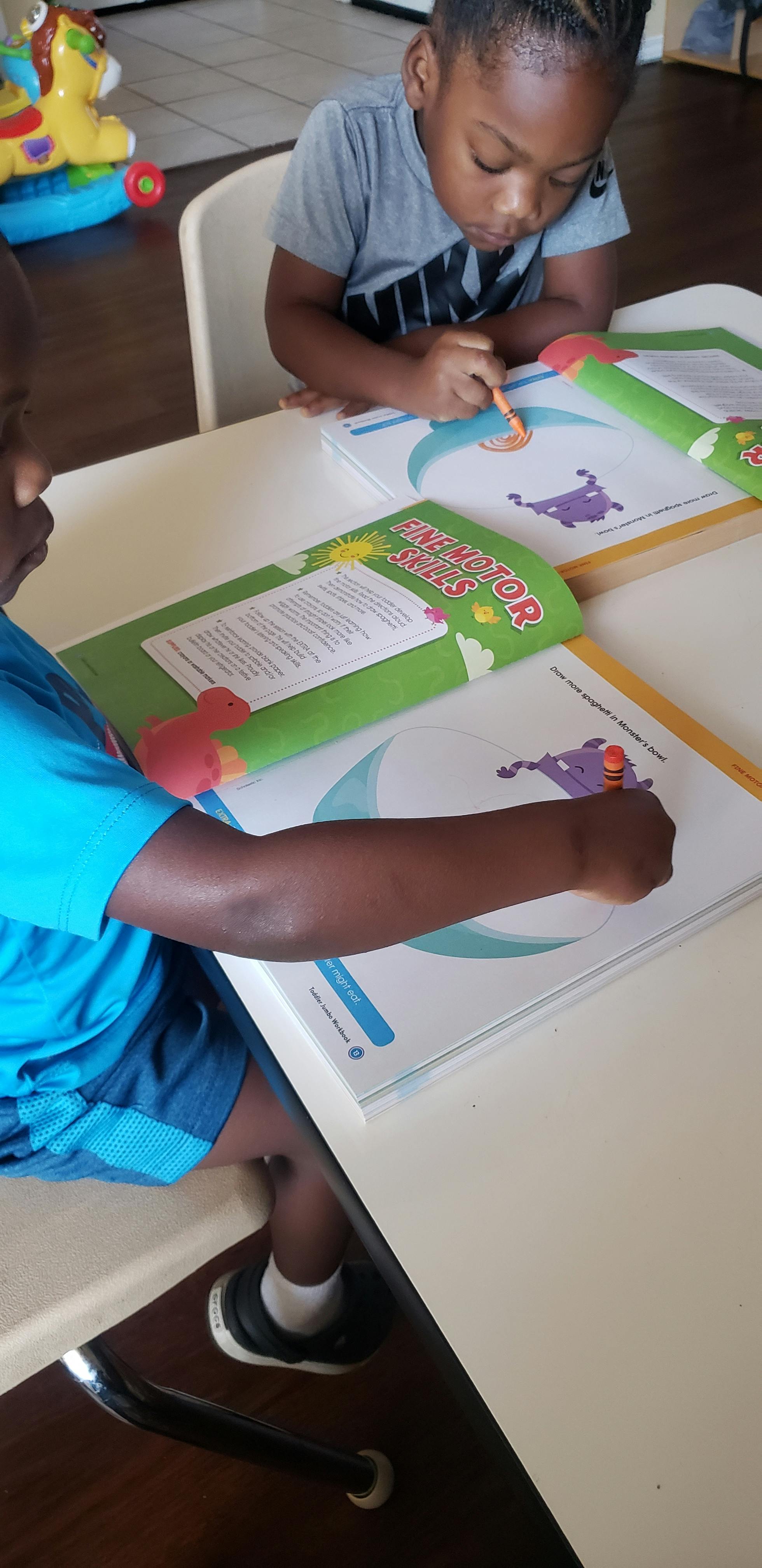 Two children drawing in workbooks at a table