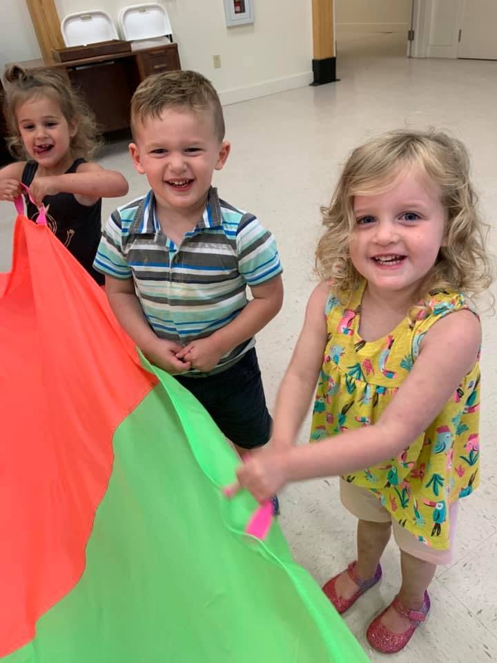 Three children playing with a colorful parachute
