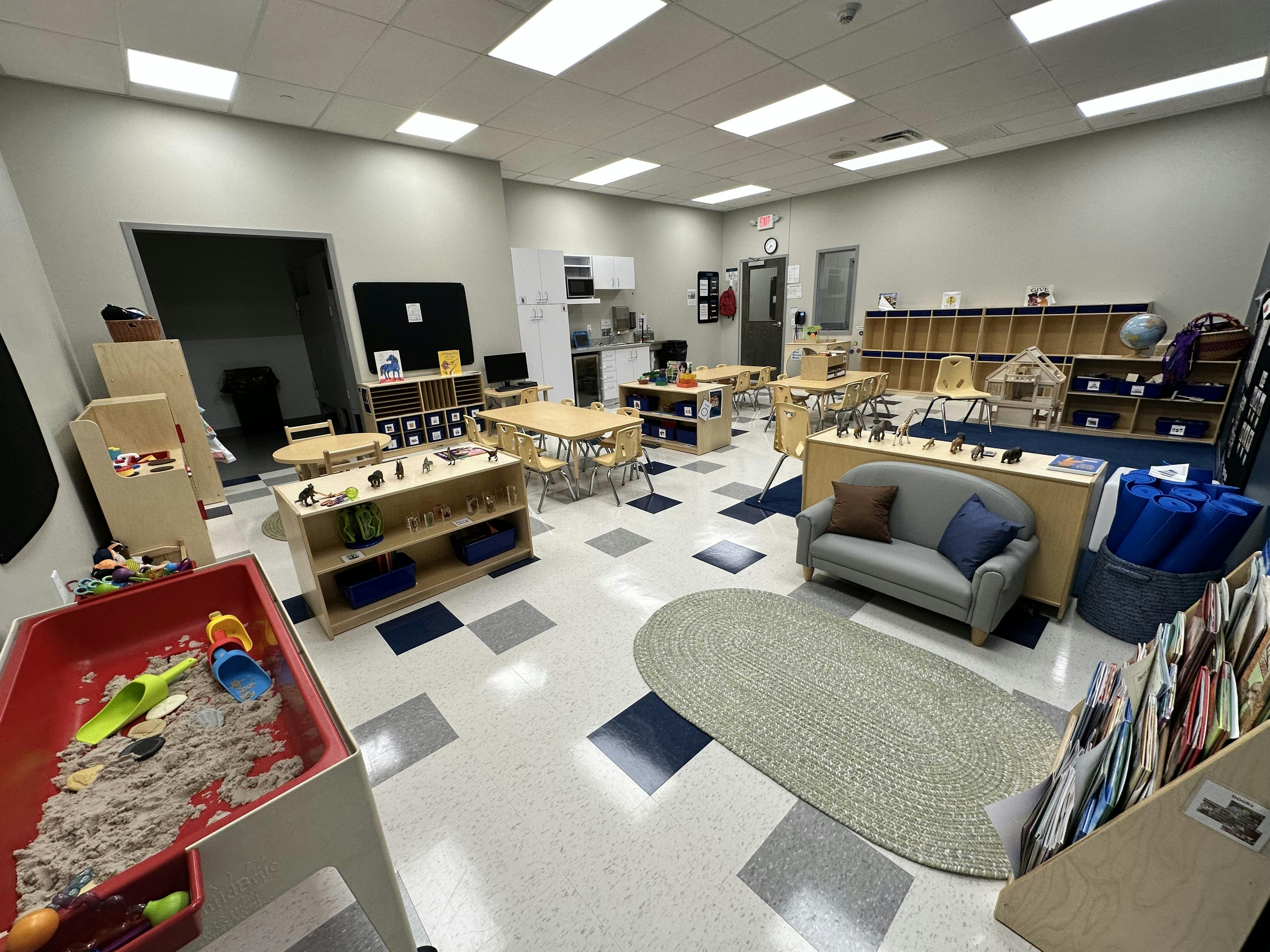 Empty classroom with small tables, chairs, and a sand play area