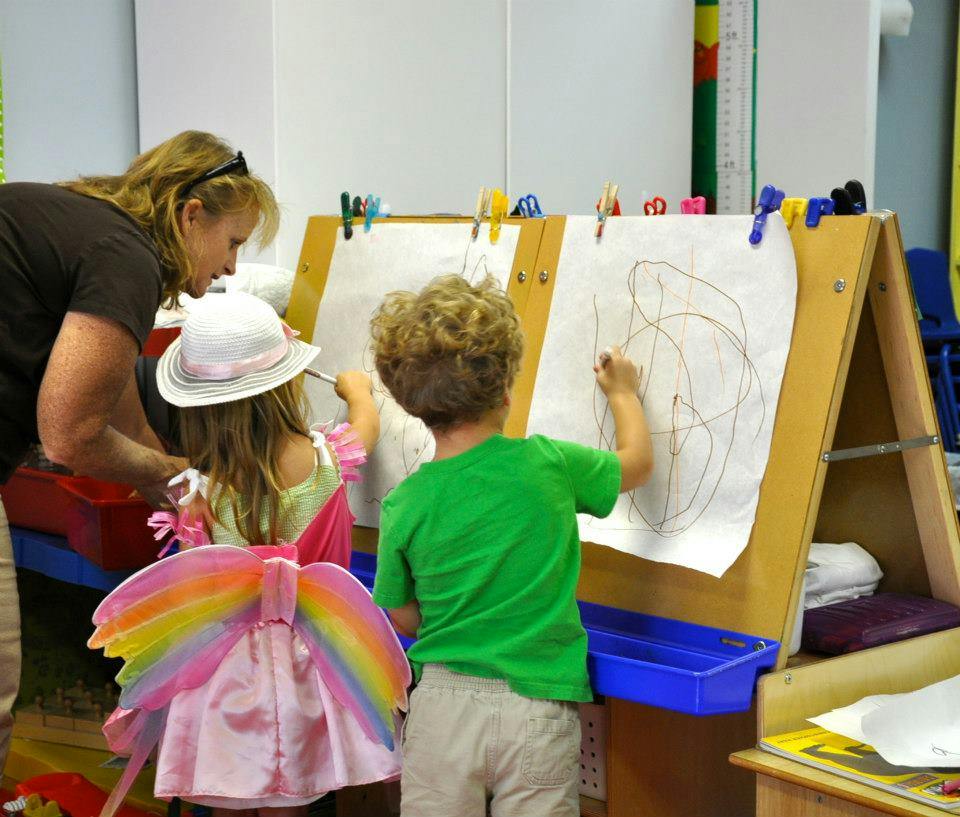 Adult and two children drawing on an easel