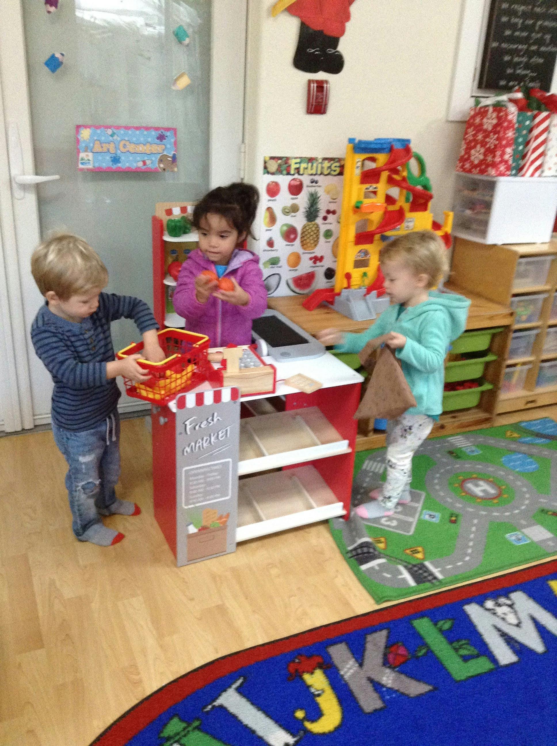 Three children playing with a toy market stand