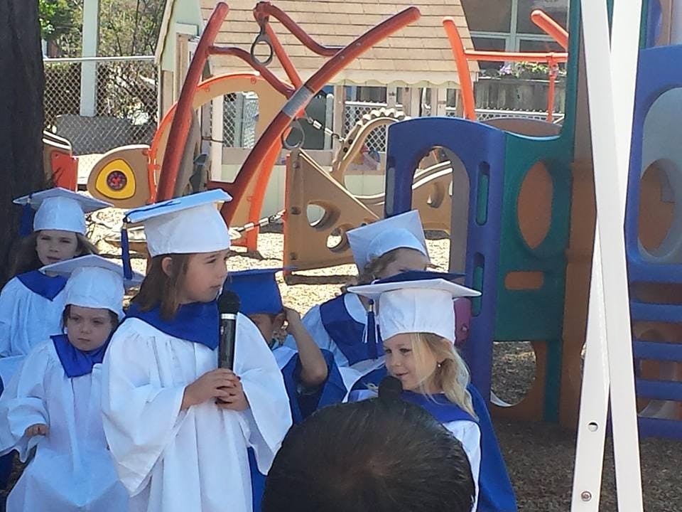 Children in graduation caps and gowns on a playground