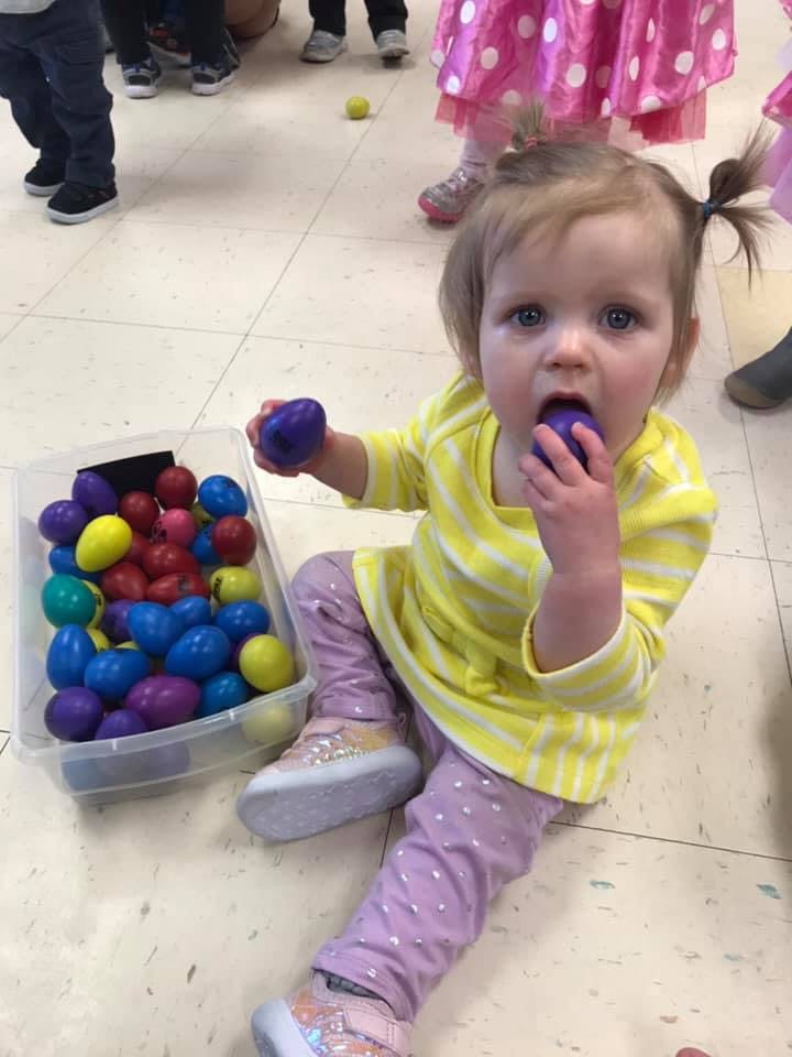 Child sitting on floor with plastic eggs, one in hand and one in mouth