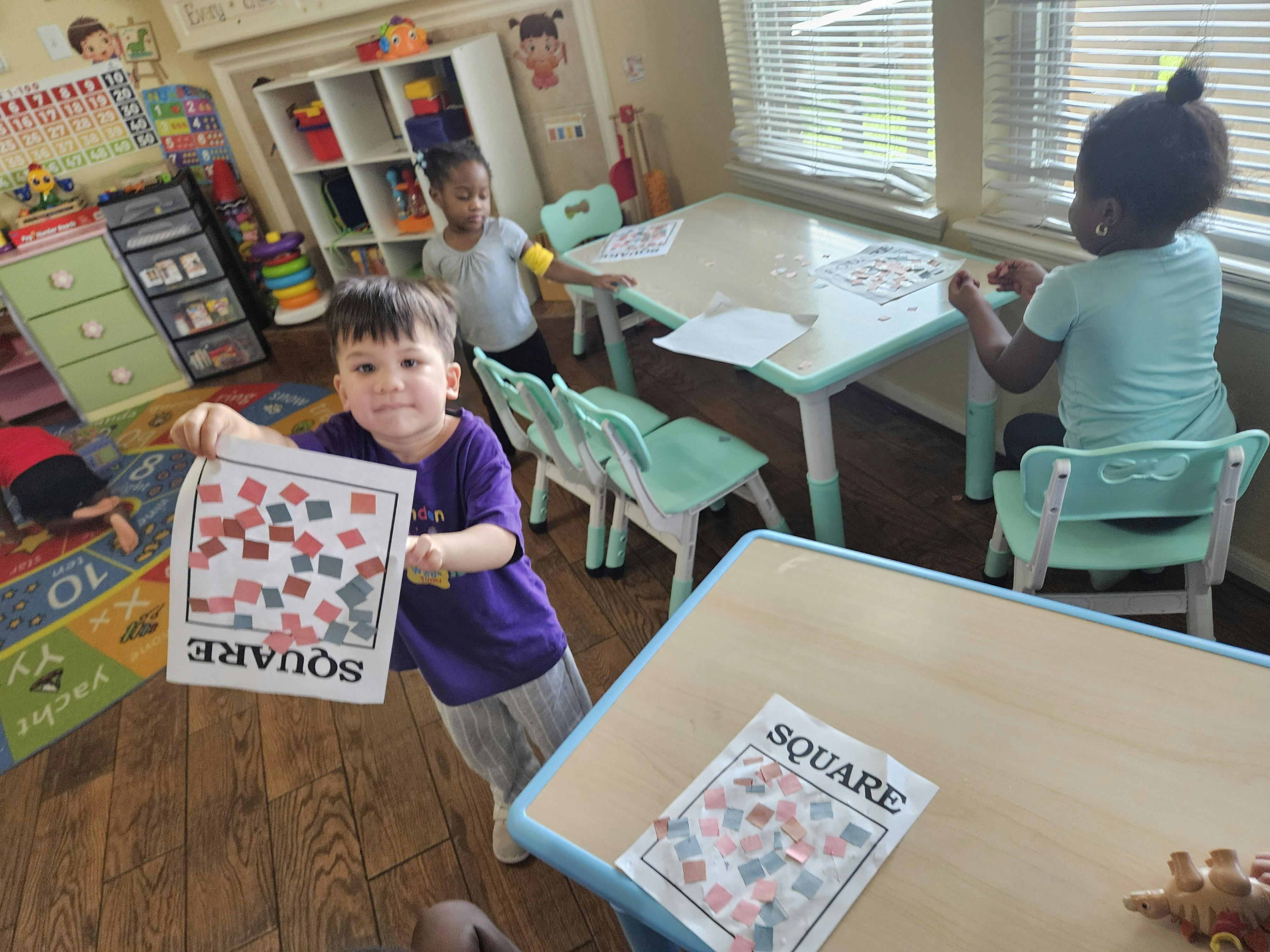 Child holding up a sheet of paper with the word square and colorful cutouts