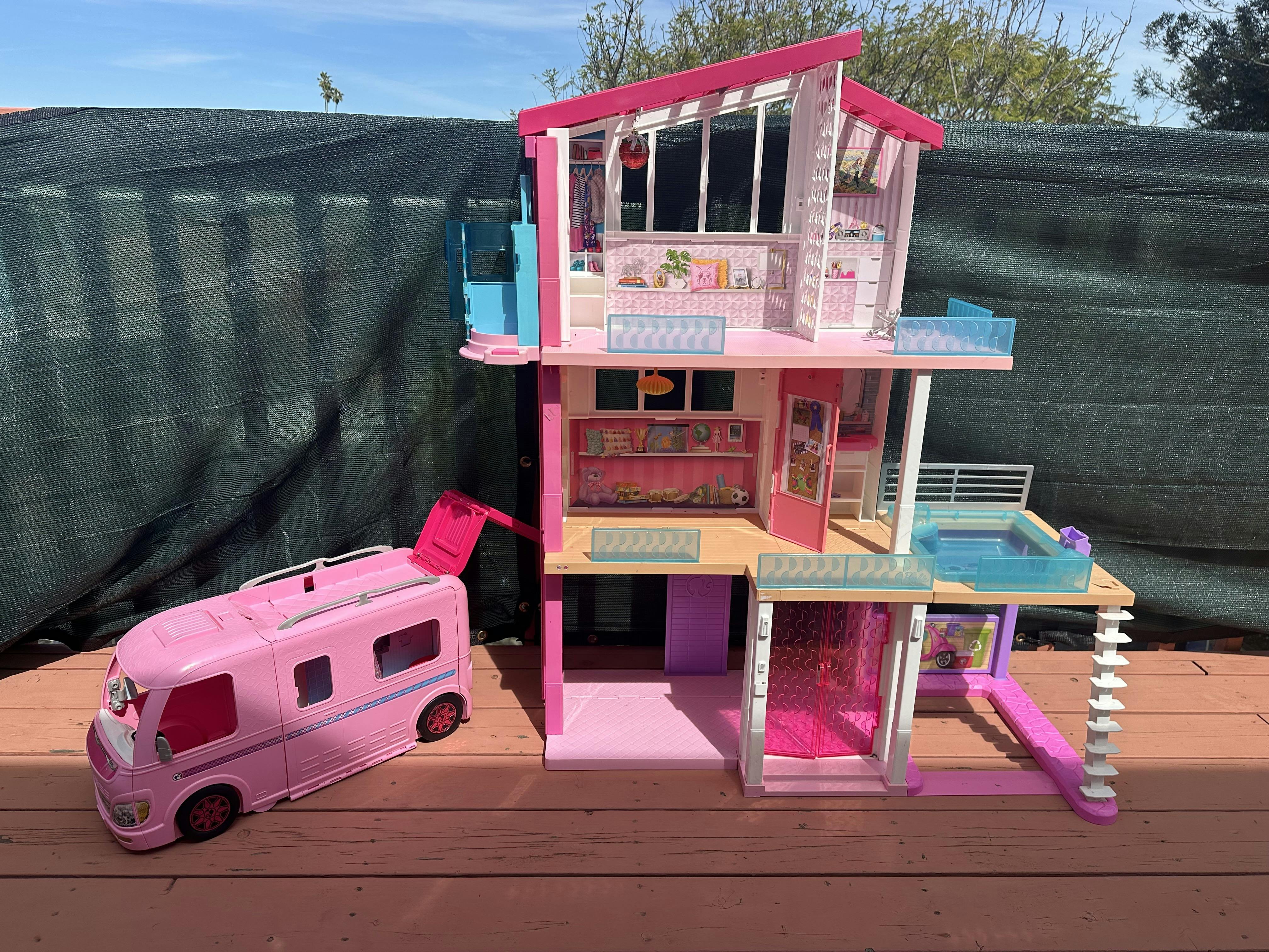 Dollhouse with a detached toy recreational vehicle on a wooden surface