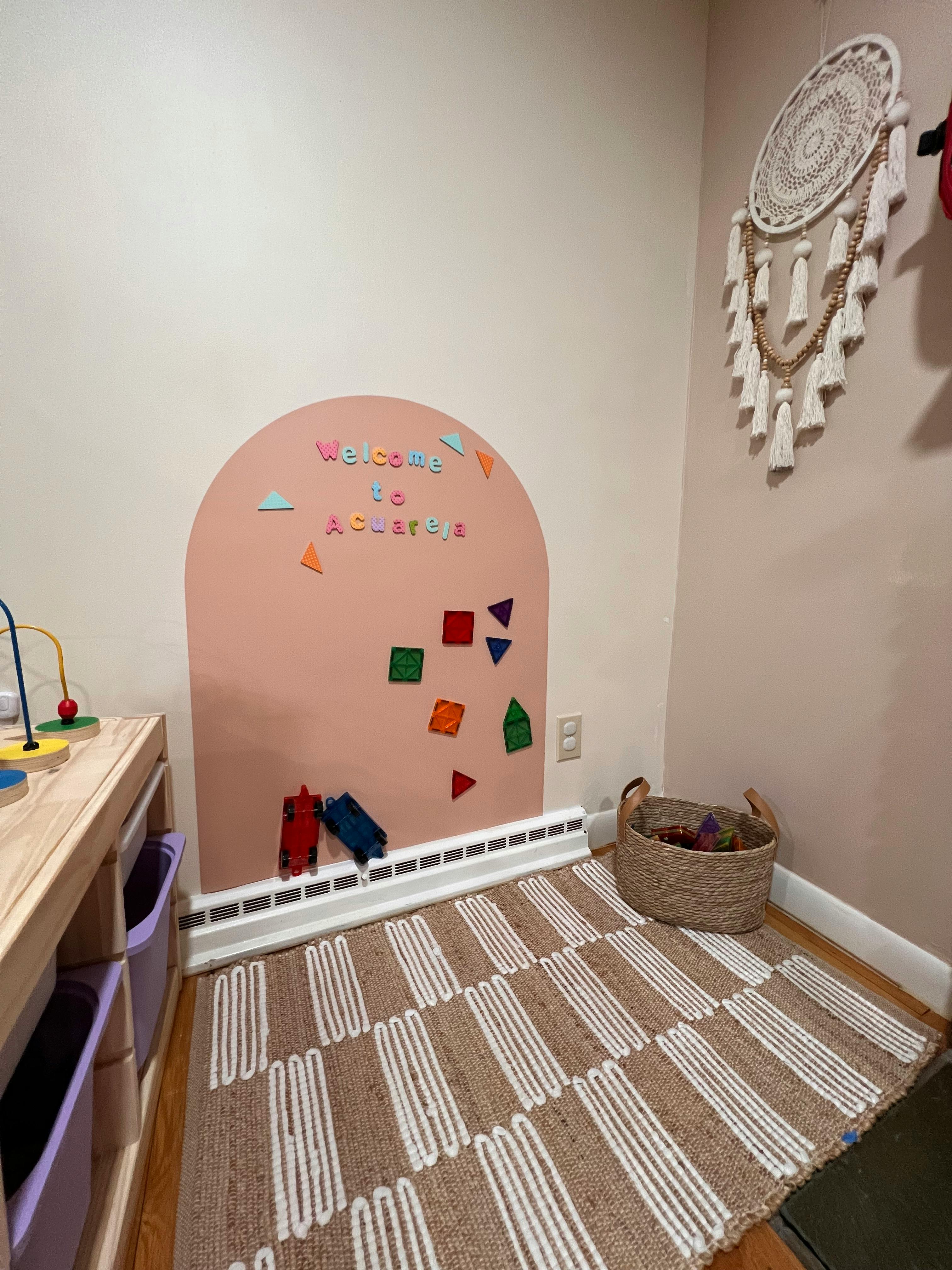 Playroom corner with a pink arch wall decal and a patterned rug