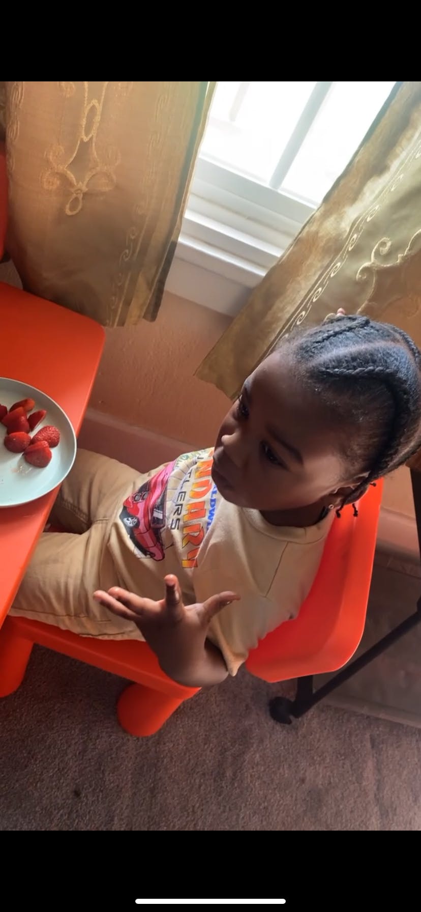 Child sitting at an orange table with a plate of strawberries