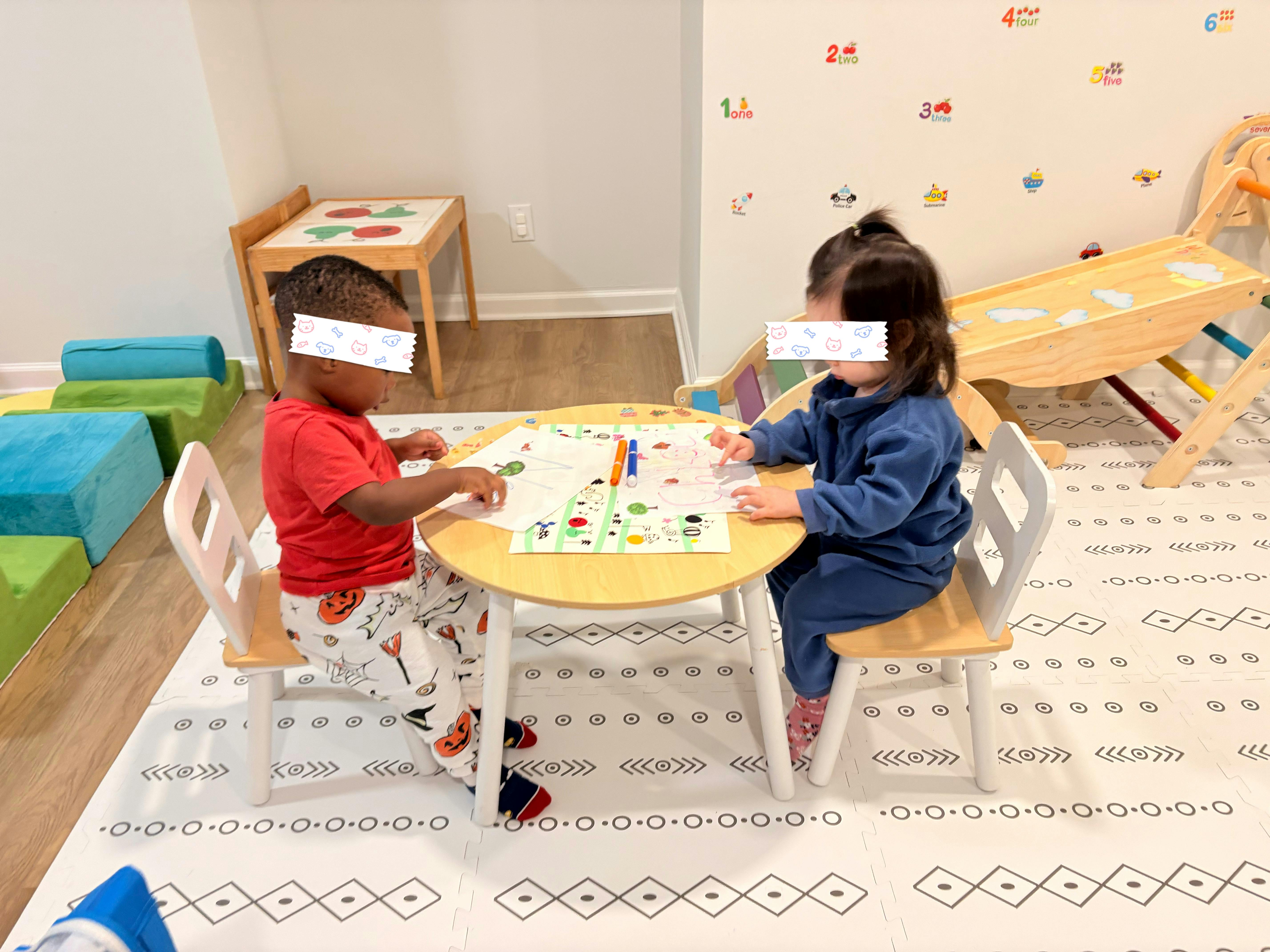 Two children sitting at a small table drawing on paper
