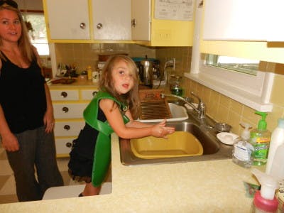 Person and child in a kitchen, child standing at a sink