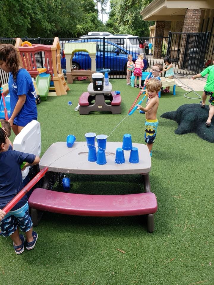 Children playing with water guns and cups on a green turf playground