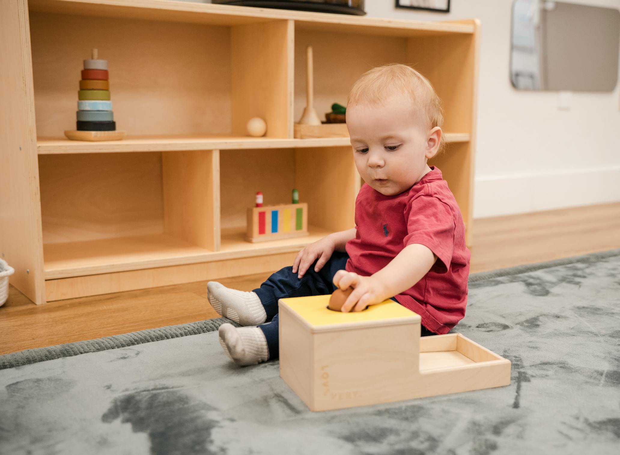 A young child sitting on a rug and playing with a wooden object toy