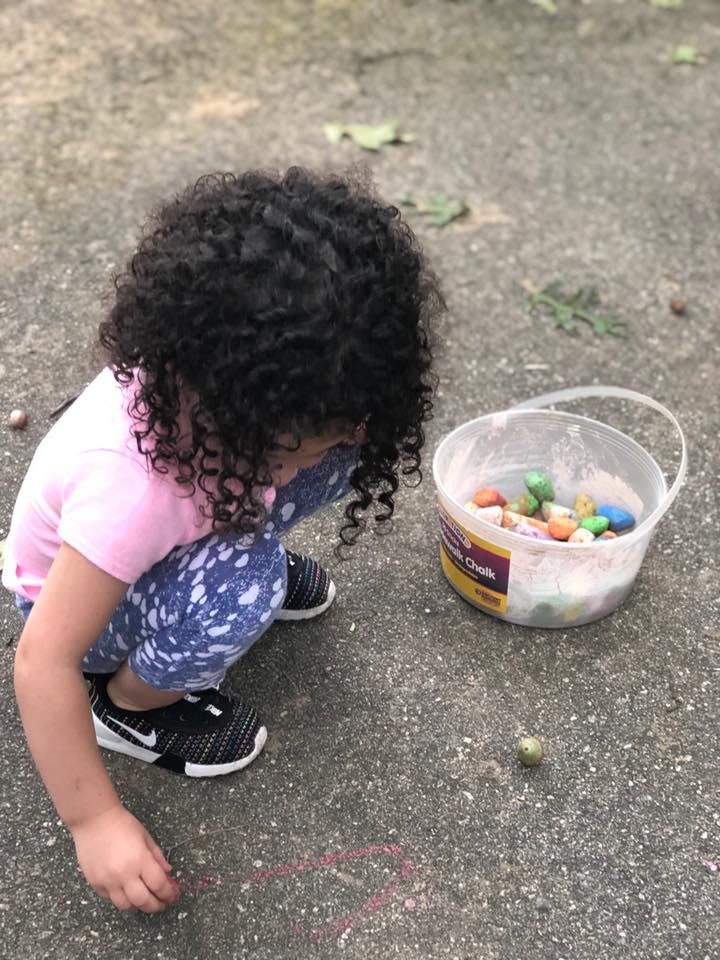 Child drawing with chalk on the ground next to a bucket of chalk