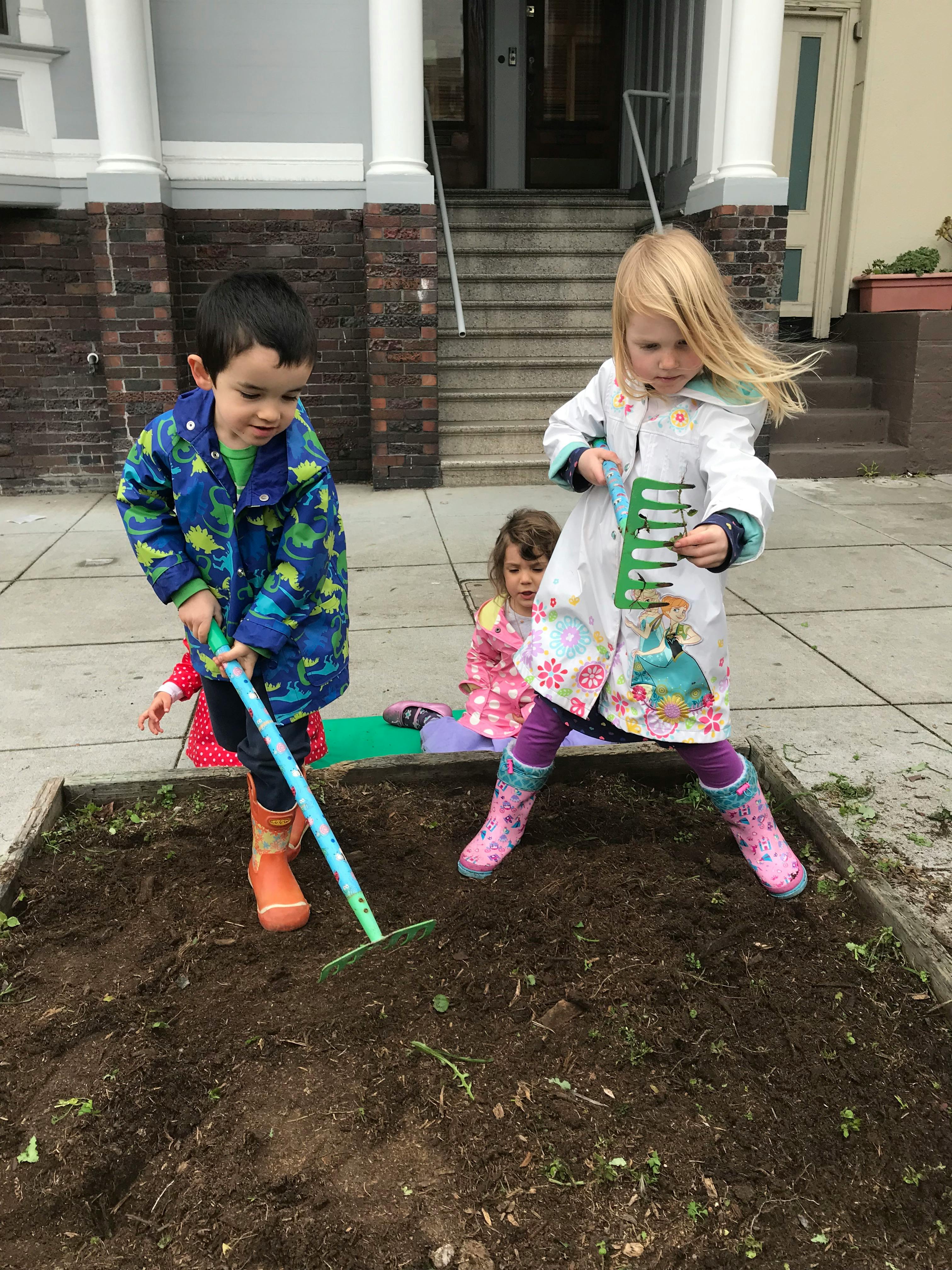 Three children playing with garden tools in a patch of dirt