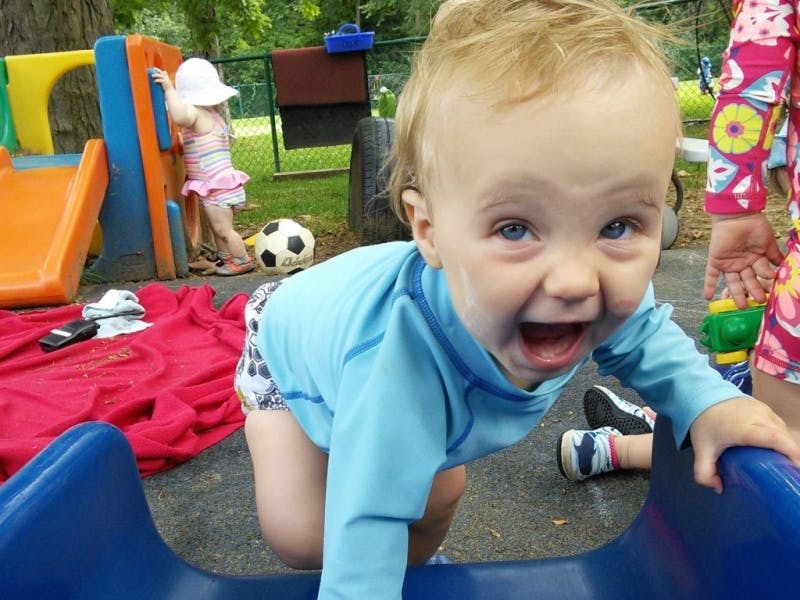 Child crawling on a blue slide with another child in the background