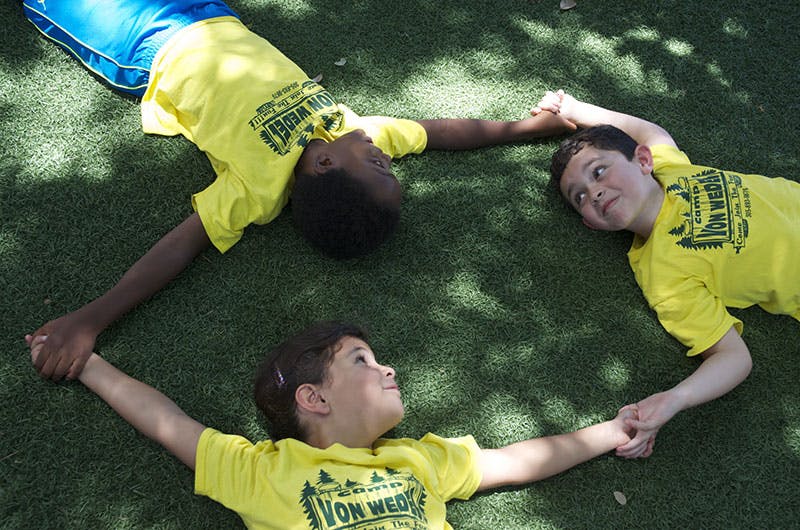 Three children lying on grass holding hands in a circle