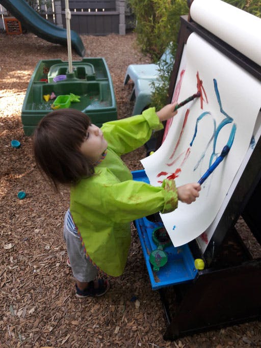 Child in smock painting on an easel outdoors