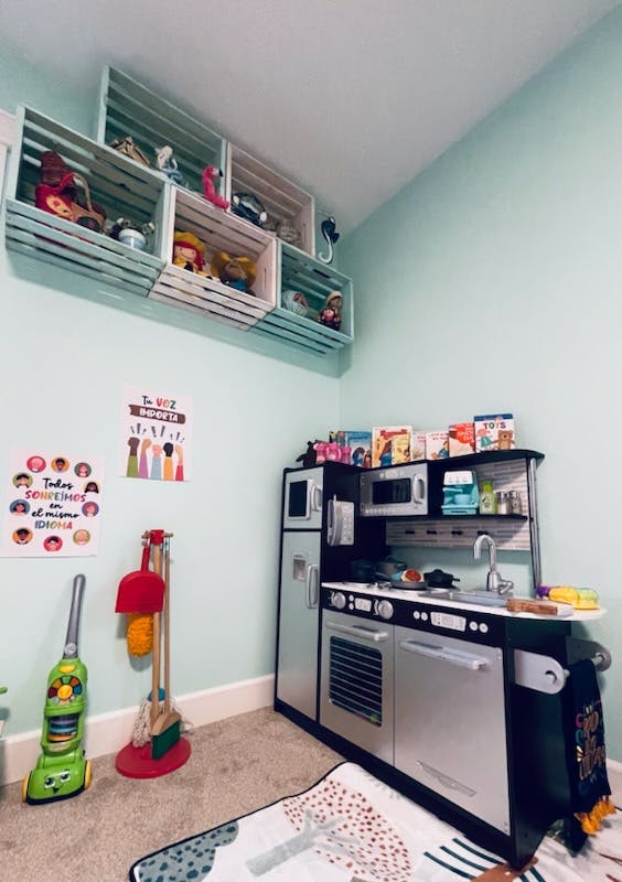 Play kitchen with toy cleaning supplies and wall-mounted storage crates