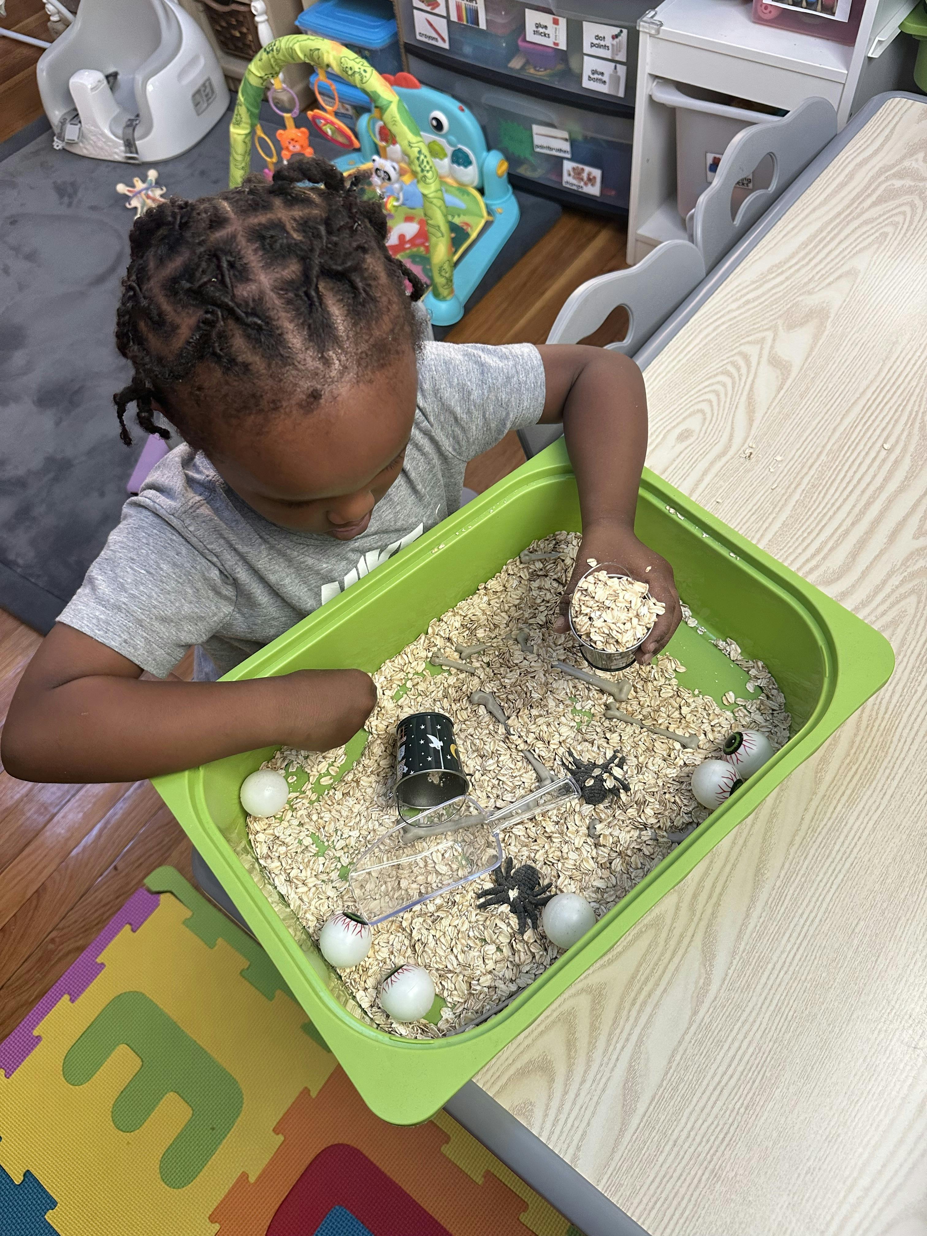 Child playing with oats and small objects in a green bin